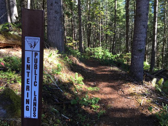 wooded trail with sign that says entering public lands in a vertical fasion.