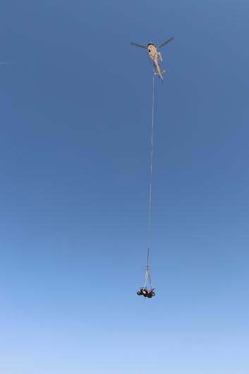 A helicopter in the air with a rope hanging from it which is attached to an ATV