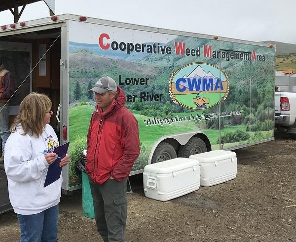 Lonnie talks to a woman with the "Cooperative Weed Management Area" truck in the background.