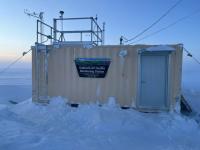 A shipping container with a trapezoid sign that reads "Bureau of Land Management Alaska Kaktovik Air Quality Monitoring Station."