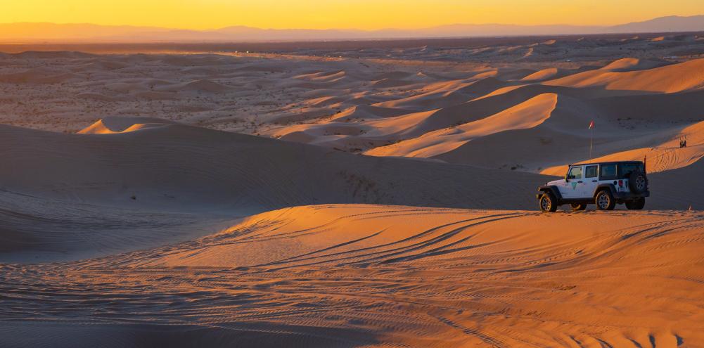Jeep overlooks sand dunes at sunset