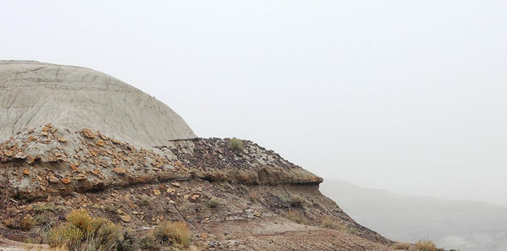 A man stands on the top of a rocky butte surveying the rocky and foggy landscape. 