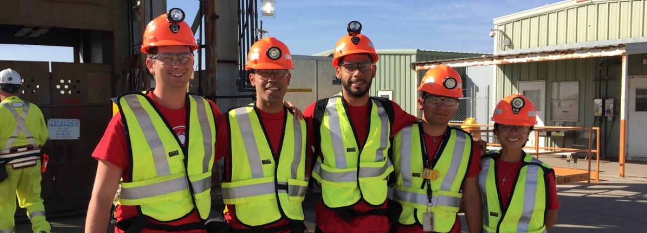 Group of five student hires smiling and wearing hard hats and bright neon vests in New Mexico