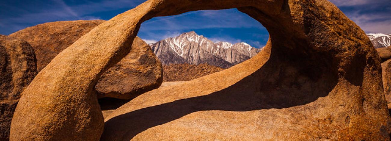 A brown, eroded arch frames Mount Whitney in the Eastern Sierras. Photo by Jesse Pluim, BLM.