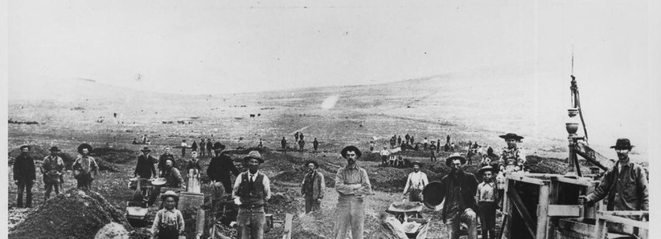 historic black and white image of men standing around mining equipment