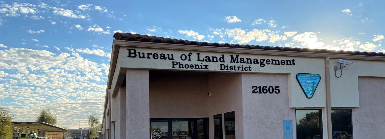 The sun rises behind a building reading Bureau of Land Management, Phoenix District. 