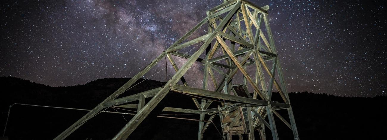 Night time picture of a mine truss with the mountains in the background and the milky way in the sky