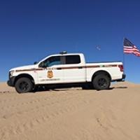 A law enforcement truck with an American flag parked on a sand dune