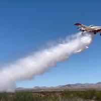 Single engine airtanker flying and dropping water on the landscape below