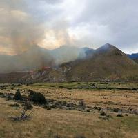 In the Slinkard Mountains, fire peaks over the ridgeline in the far distance as smoke fills the sky.  Photo by Troy Maguire, BLM.