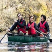 A group of smiling people who are all wearing life vests and paddling their green canoe.