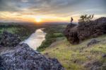 Woman standing on a rock overlooks sunset over river