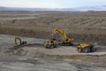An excavator loads material into a large dump truck as another dump truck waits to be loaded.