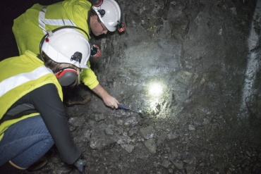 Two individuals wearing hard hats examine an underground deposit.