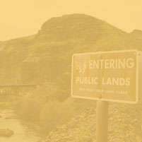 A BLM sign that reads 'Entering Public Lands' near a river with a railroad crossing
