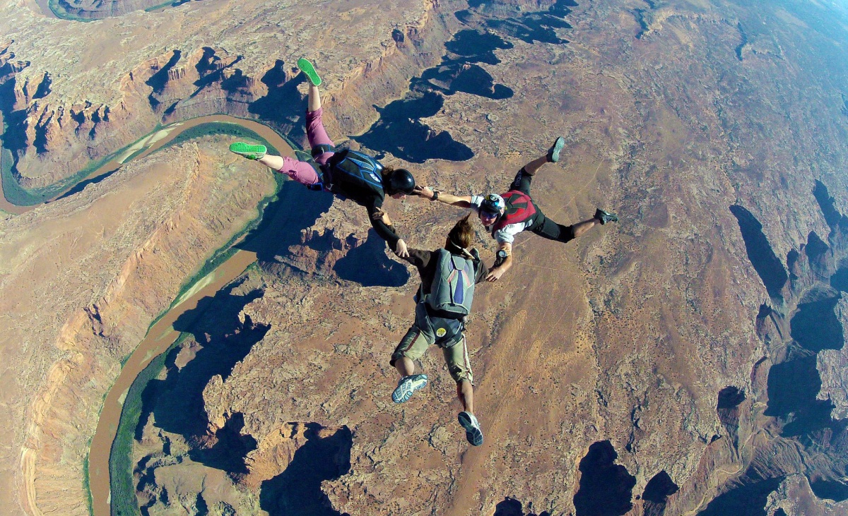 Three skydivers link arms mid-drop. 