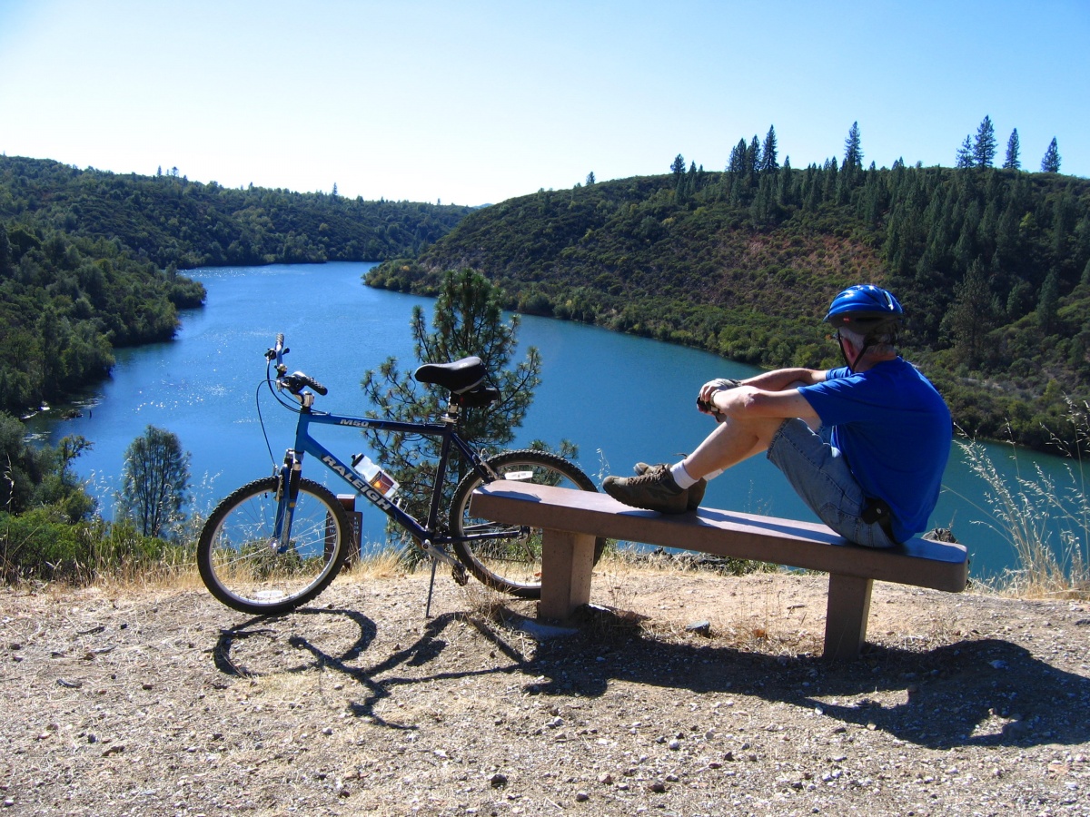 A bicycle rider takes a break on a bench at a river overlook. 