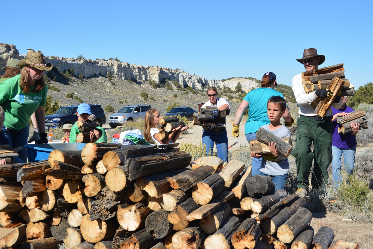 group of children and adults pick up firewood and stack in a large pile.