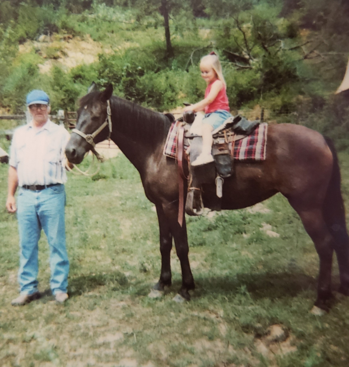 Man standing next to horse with girl on back. 
