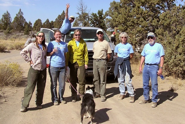 group of several folks posing near a truck in a treed landscape