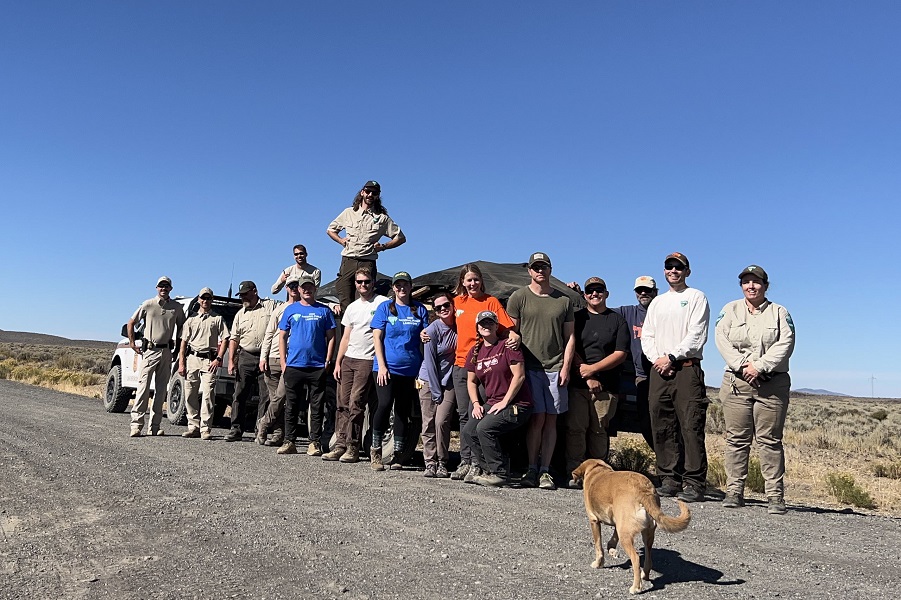 group of several folks posing near a truck with a dog