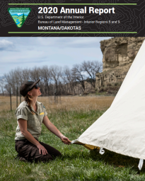 Woman sitting on grass holding the bottom of a Teepee to stake it down. Cover image for 2020 Annual Report. 
