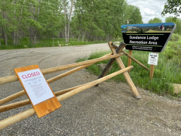 Wooden fence with CLOSED sign blocking road. Sundance Lodge Recreation Area sign on the side of the road. 