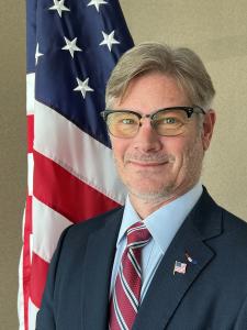 A portrait of Eric A. Kriley in front of an American flag