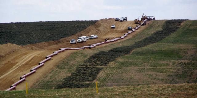 A dirt road goes through the center and a line of large pipes is alongside.