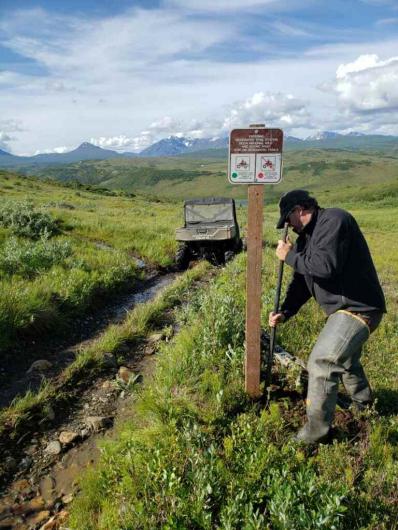 Man digging near sign post.