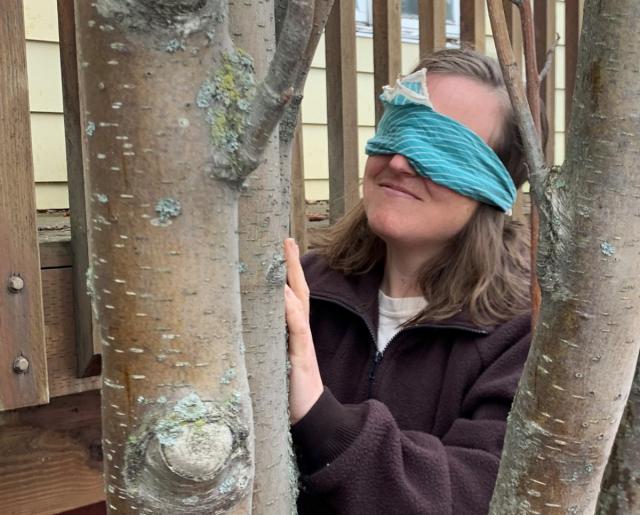 Blindfolded woman smiling at tree.