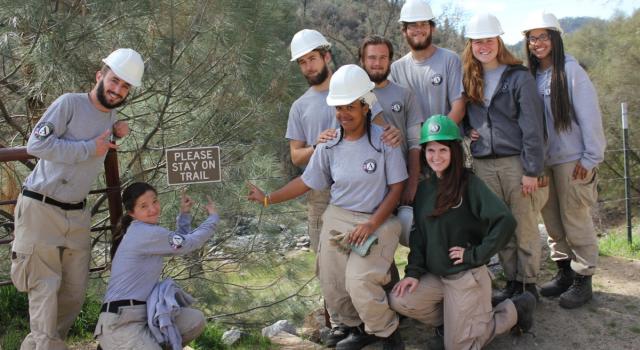 Group of AmeriCorps wearing hard hats and posing for group photo during trail work.