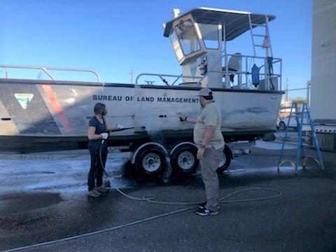 Two people use a pressure washer to clean a boat