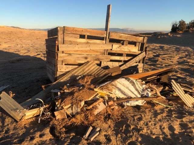 Broken boards, chicken wire and other refuse put in a recreation area with the shadow marking the landscape.