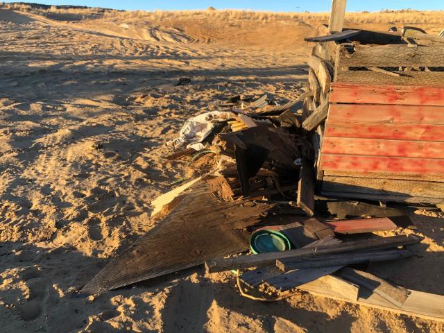 Broken boards, chicken wire, and other refuse put in a recreation area with the shadow marking the landscape.