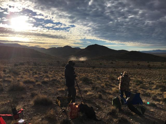 Members of the public (foreground) watch as the helicopter pilot (background) shepherds wild horses toward the trapsite.