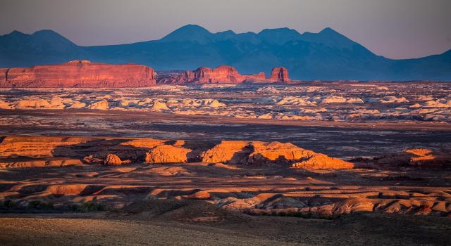 Labyrith Canyon Wilderness as the sun is setting. Outlines of mountains appear in the background and vibrant colors are shown on the lands. 