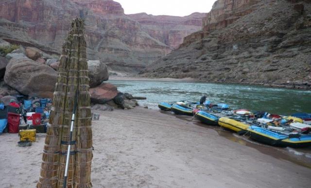 a tule raft stands upright on a beach near other rubber rafts on the shore