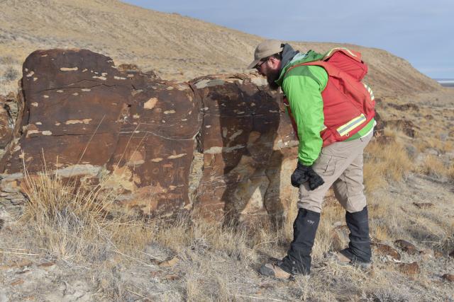A BLM Utah staff member looking at an archaeological site on a rock. His shadow covers part of the rock as he bends down to look at the site.