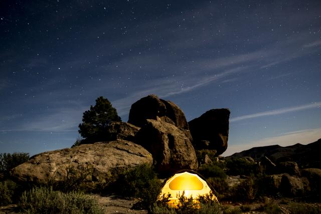 Illuminated tent near a rocky background and starry night