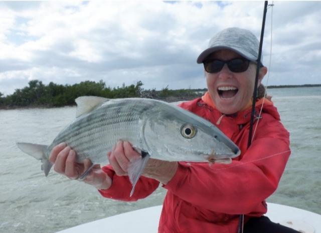 Jamie Connell, wearing a ball cap and red rain coat, holding a bonefish caught fly fishing