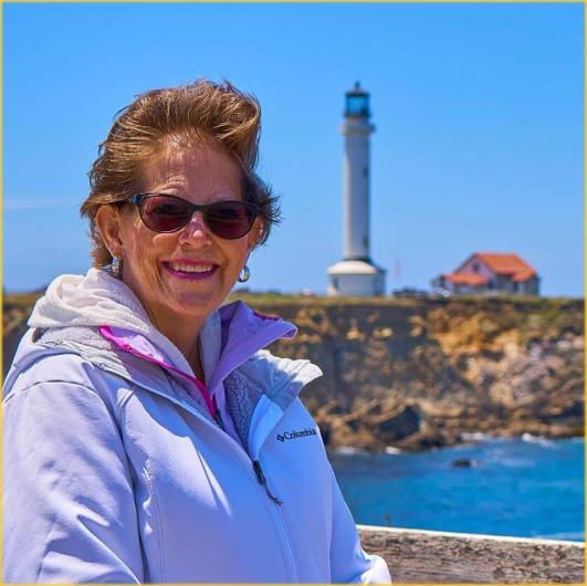 Pam smiles in front of the Point Area Lighthouse in California, which is surrounded by BLM-managed public land.