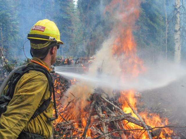 Wildland firefighter sprays burning pile of logs