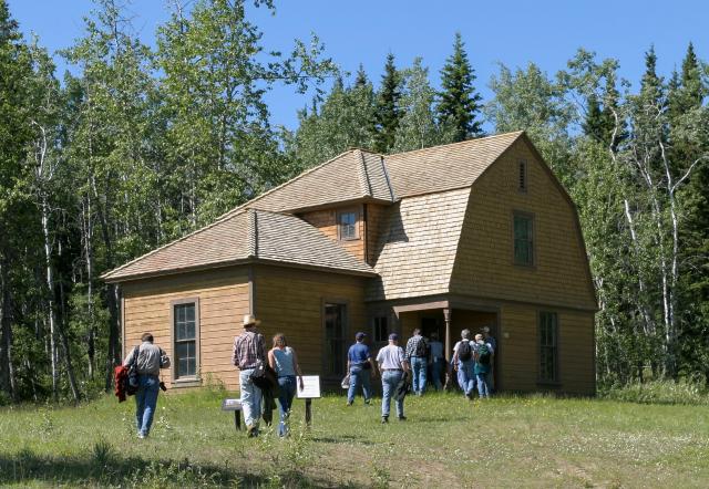 A group of visitors walk toward a two-story wooden house.