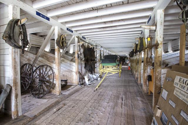 A long barn includes numerous stables, a wagon, and artifacts.