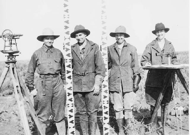 A black and white photo of four women in a line, proudly smiling with their surveying equipment