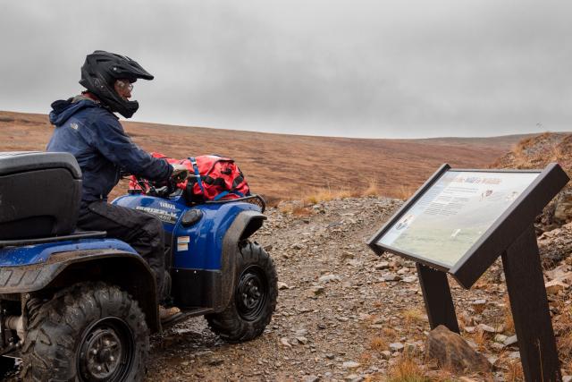 Person on an OHV in the mountains reads an information kiosk. 
