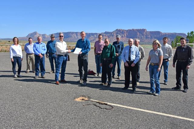 a group of people on an airport runway. Red cliffs are in the distance.