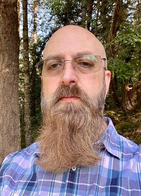 photo of person with glasses and beard standing near trees