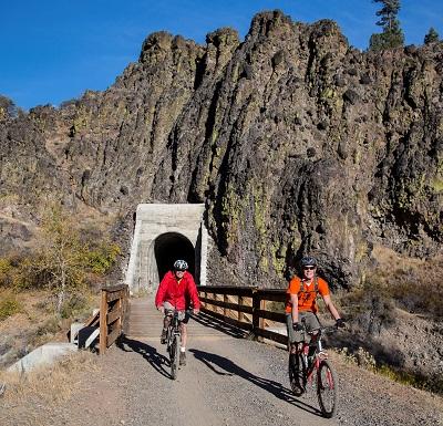 Two  cyclists emerge from a rail tunnel. 